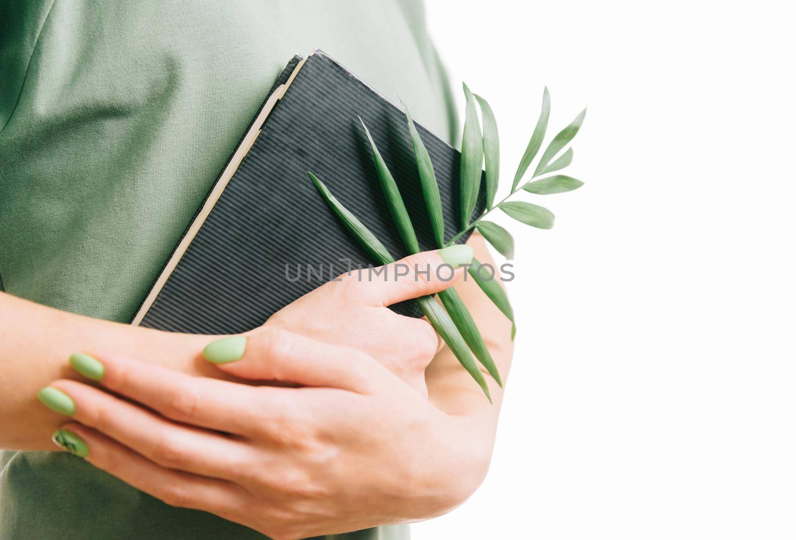 Unrecognizable woman with green manicure holding a notepad and palm leaf.