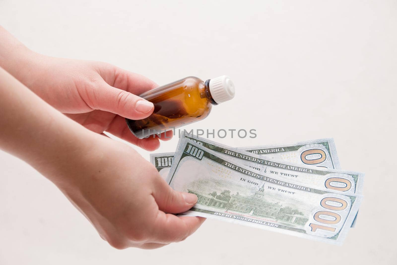 female hands holding a bottle of medicine and dollars notes on a white background