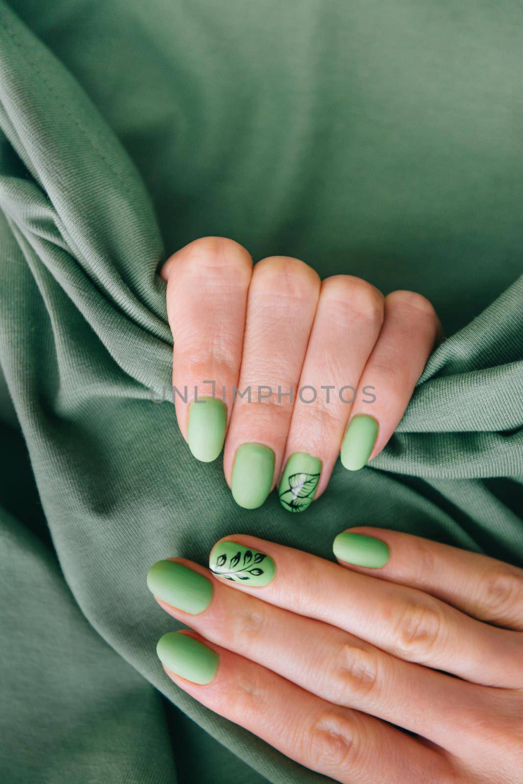 Female hands with art nails design and summer style manicure of green color on cotton fabric background.