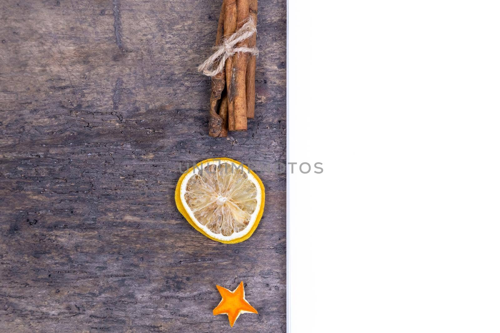 A pile of cinnamon sticks, dried orange and tangerine stars on old wooden table with white empty piece of paper. Christmas decoration. Christmas card by lunarts