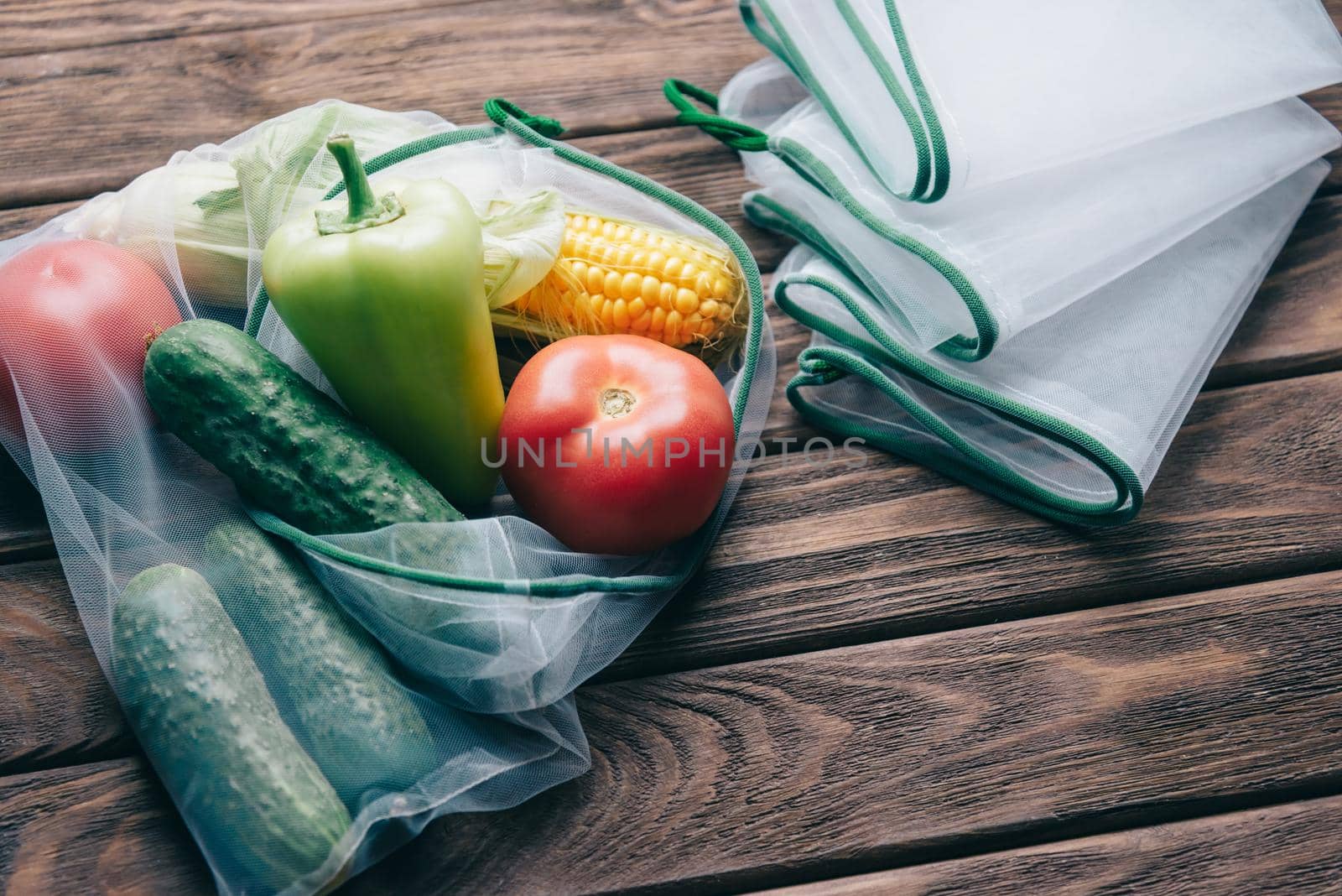 Different fresh vegetables in reusable eco bag near empty mesh package on a wooden background. Zero waste and free plastic concept.