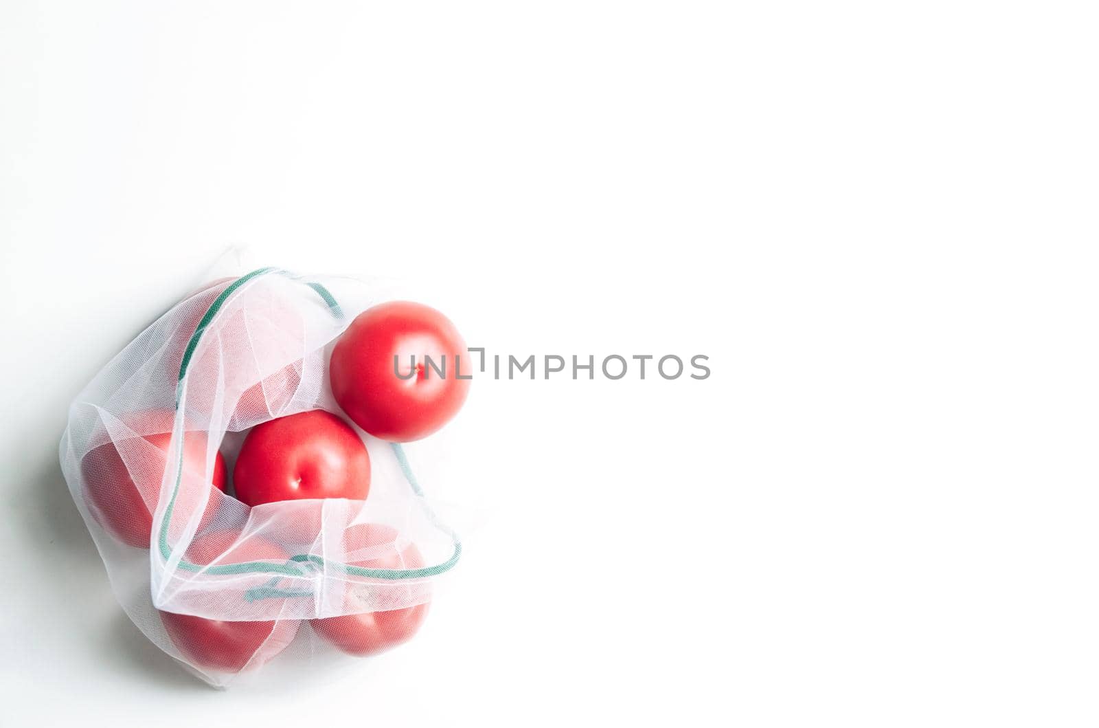 Reusable eco mesh bag with fresh tomatoes on a white background, top view, copy-space. Zero waste and no plastic concept.