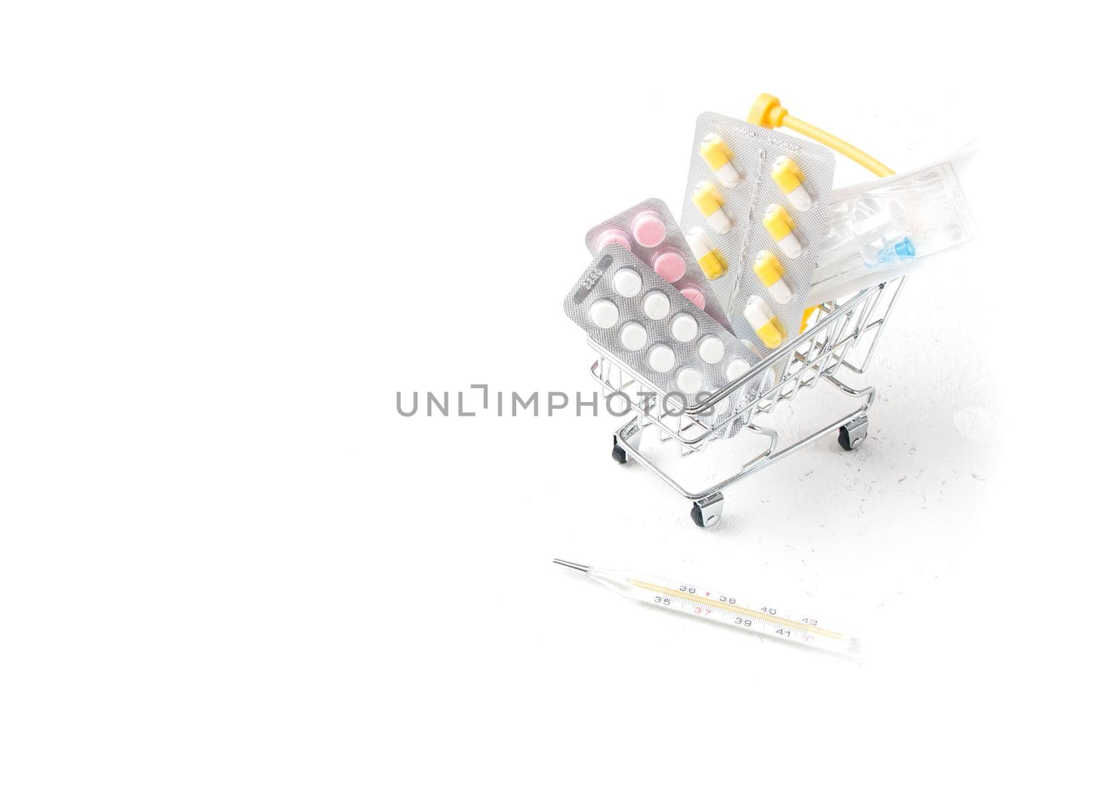 medicines in a shopping trolley and mercury thermometer on a white background copy space