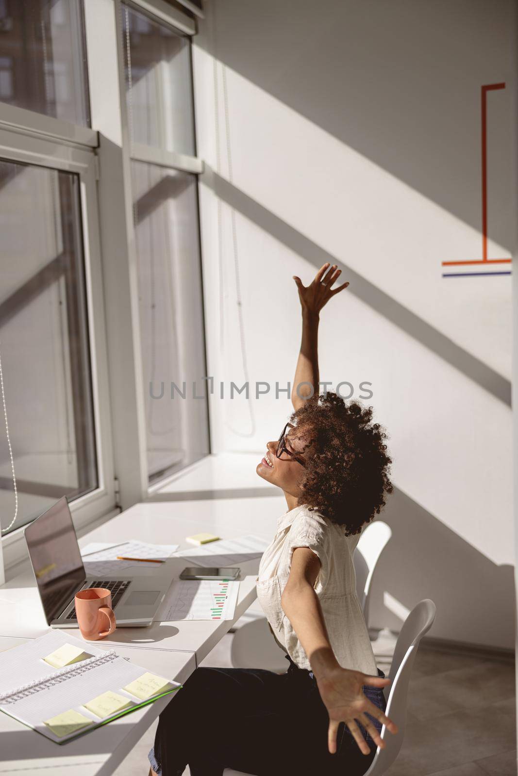 Happy Afro American woman stretching at the desk in the office while sitting near th window