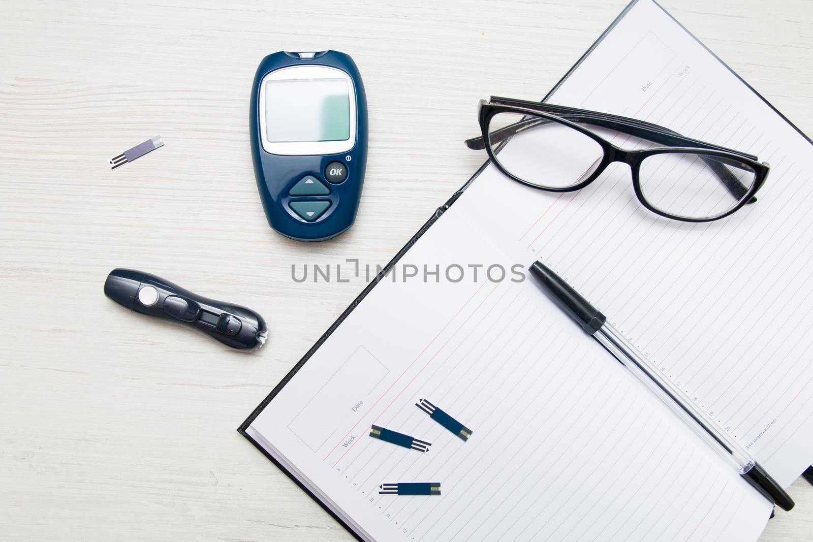 glucose meter, blue glucometer lies on a table next to a notebook, glasses, pen and syringe for measuring blood sugar, diabetes concept by natashko