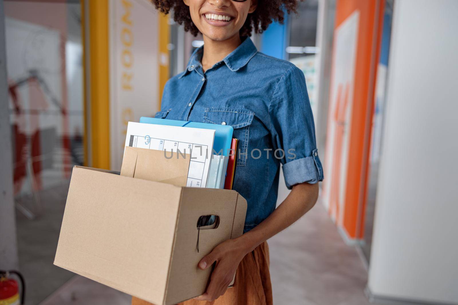 Cropped photo of young lady holding box with documents while walking along the office corridor