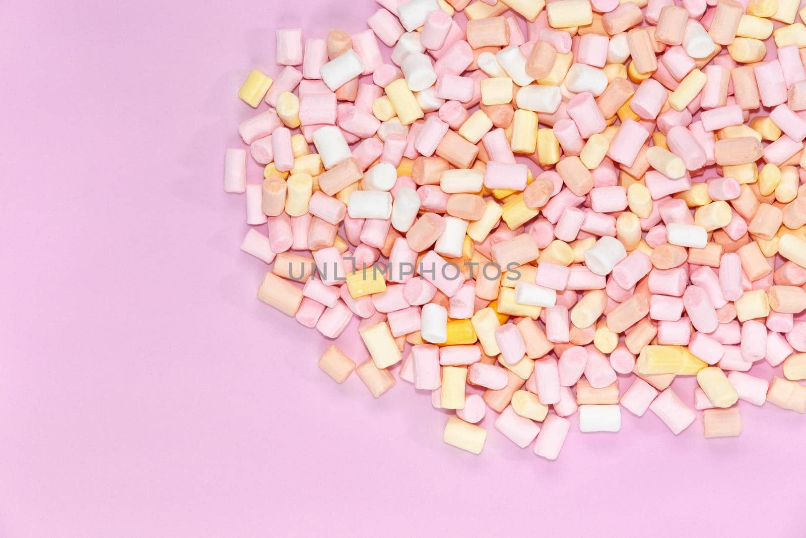 Top view on multi-colored marshmallows on a monochrome pink background.