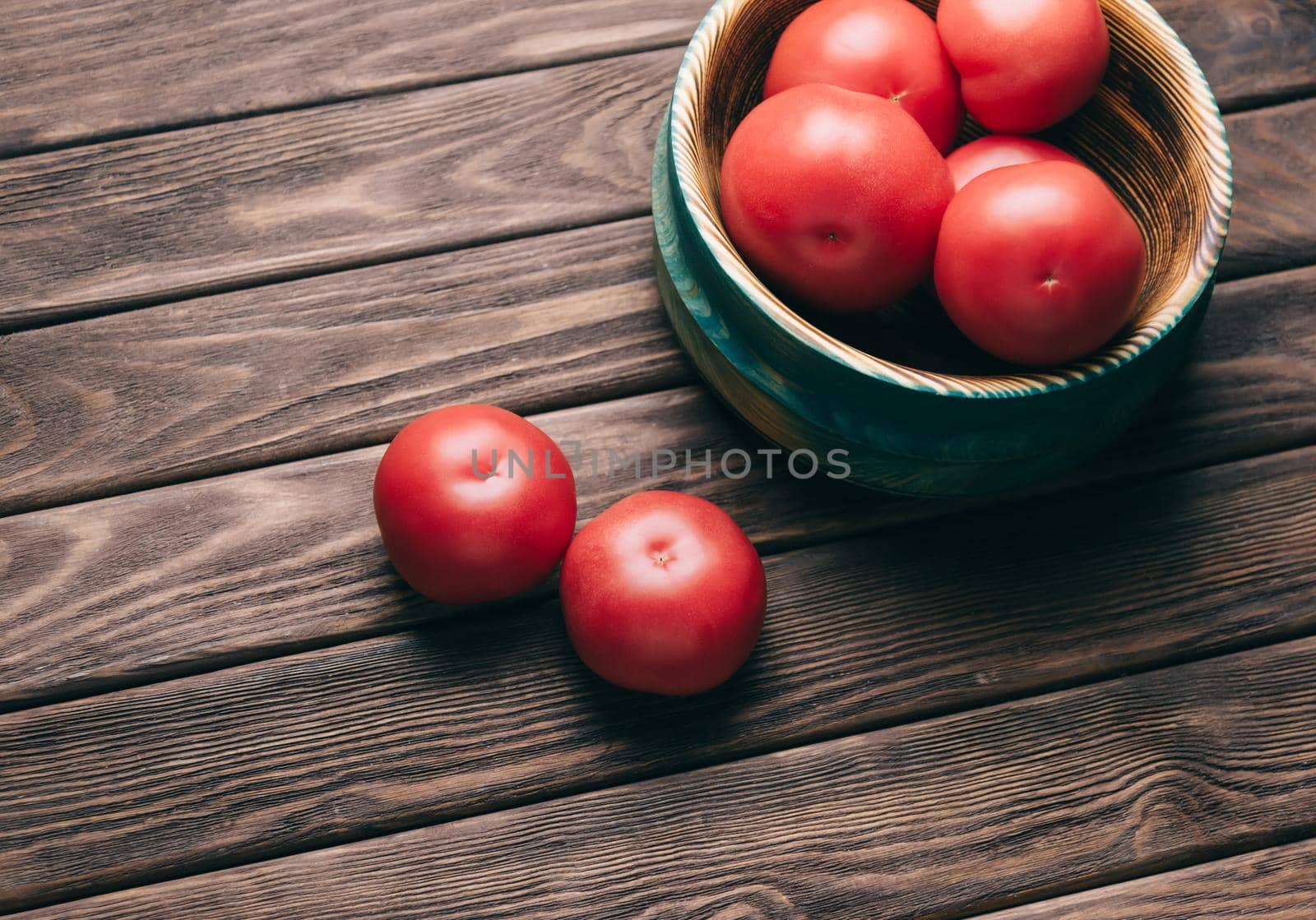 Fresh red ripe tomatoes in a bowl on a wooden table.