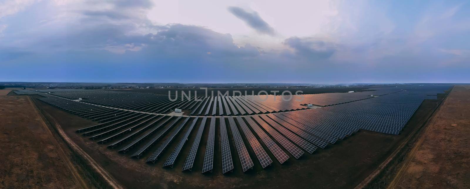 Aerial panorama view of large solar panels at a solar farm at bright summer sunset. Solar cell power plants, colorful photo