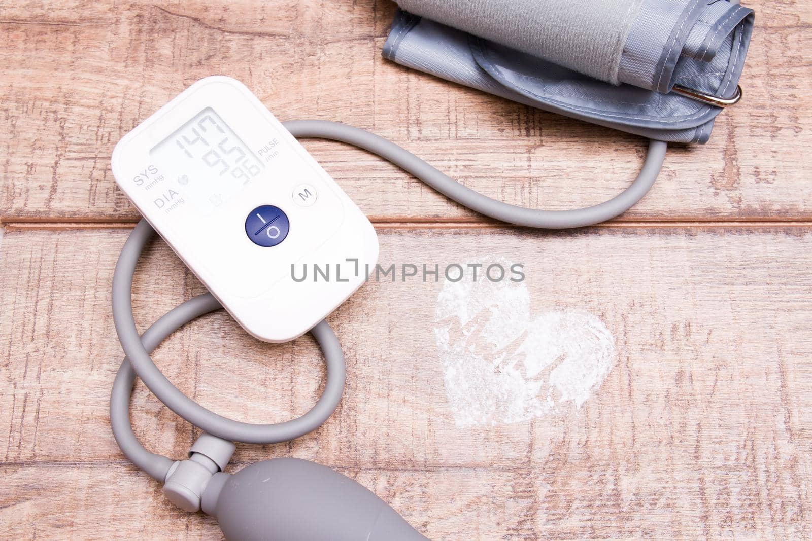 blood pressure monitor on wooden background, heart made of white powder, pulse drawn, copy space, top view, heart pressure concept