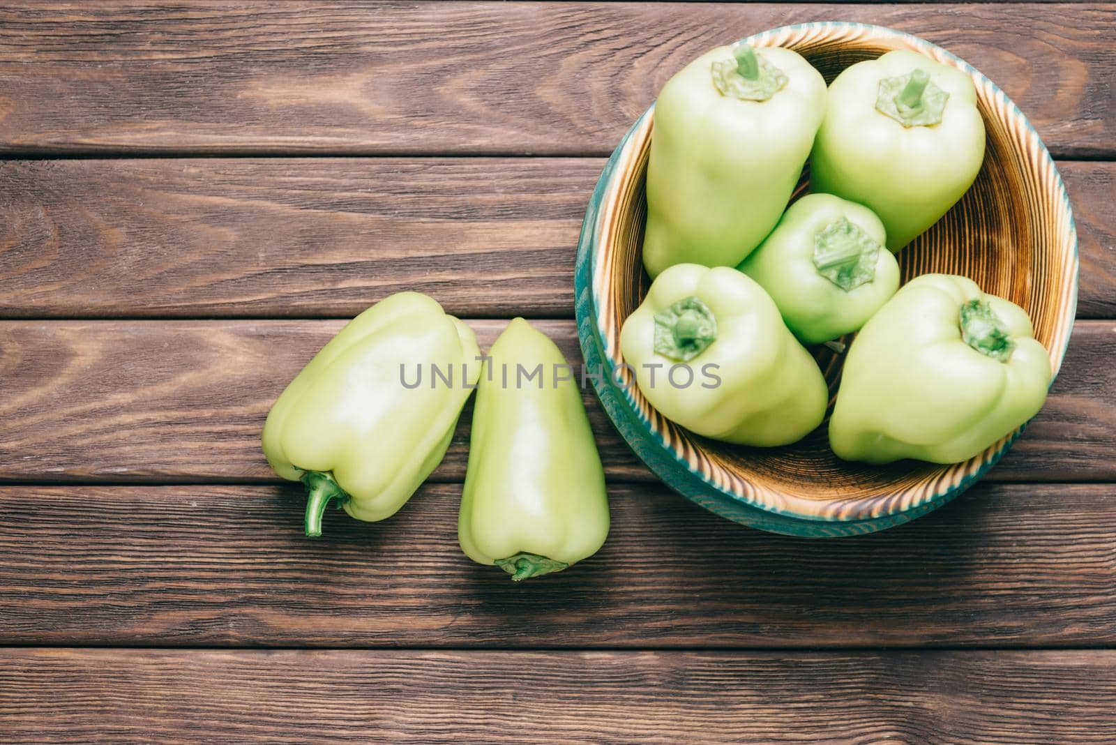 Fresh green peppers in bowl on wooden table, top view.