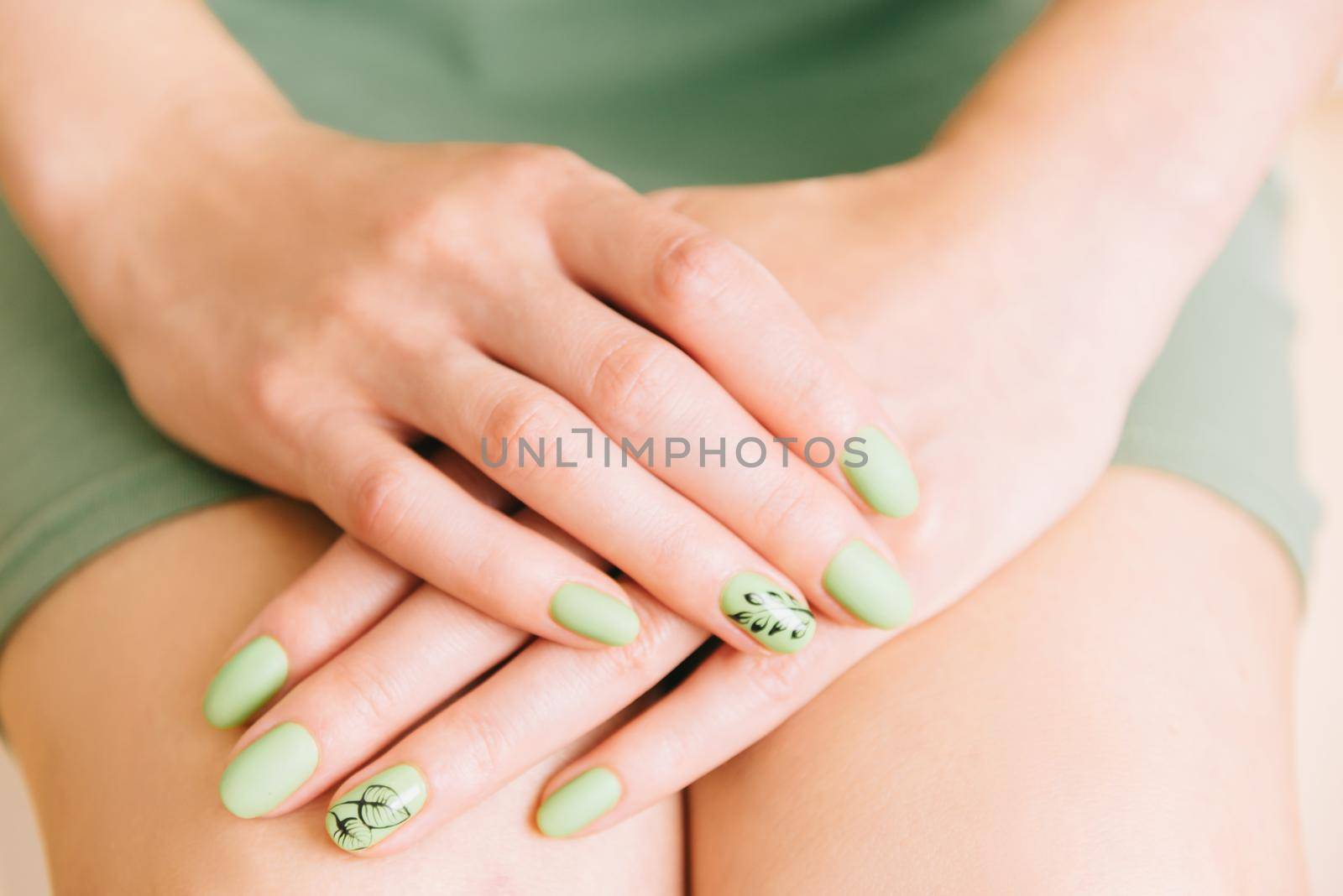 Woman holding hands on her knees. Female trendy nail-art manicure of green color.