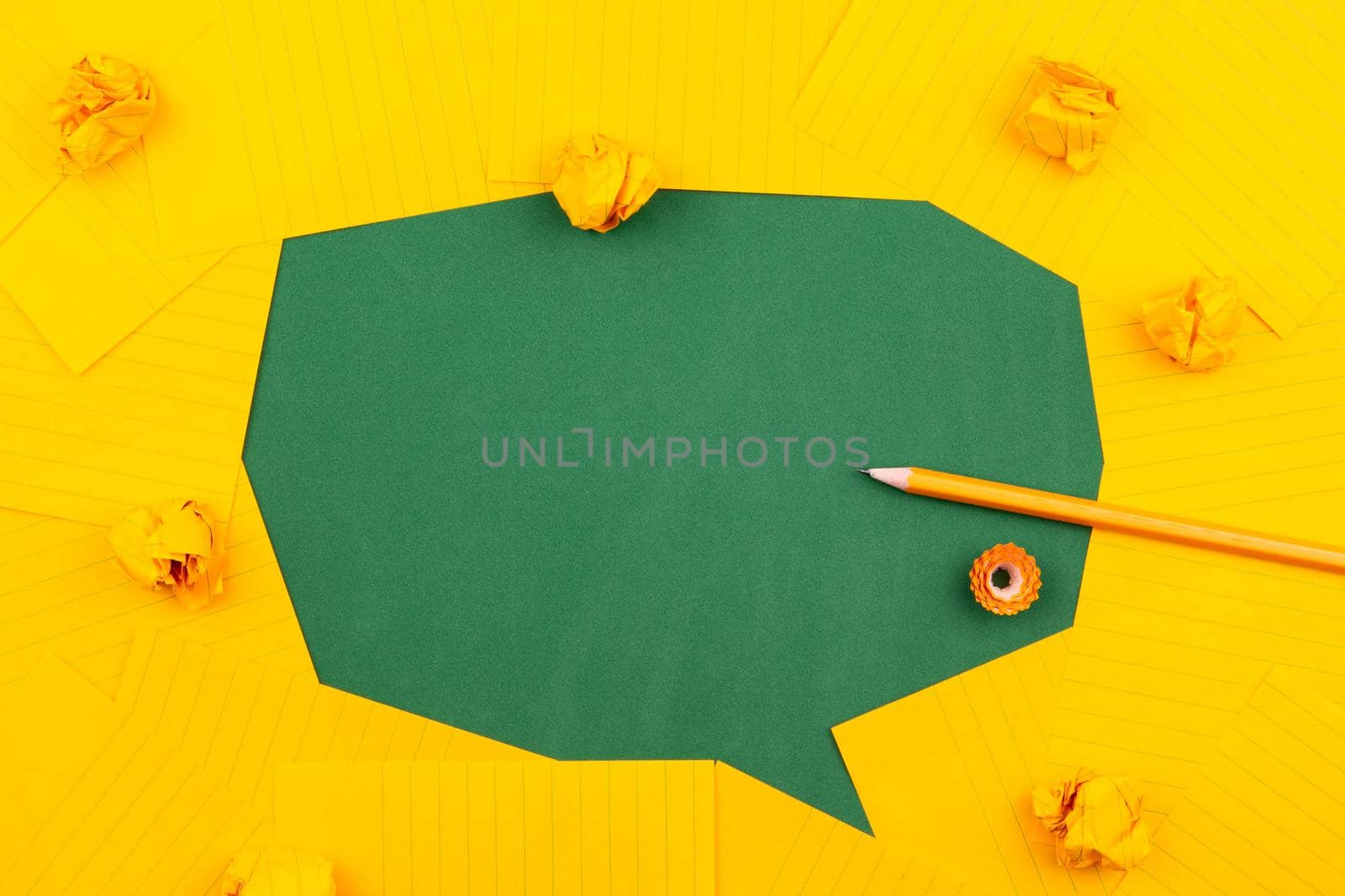 orange sheets of paper lie on a green school board and form a chat bubble with pencil, crumpled papers and copy space for text