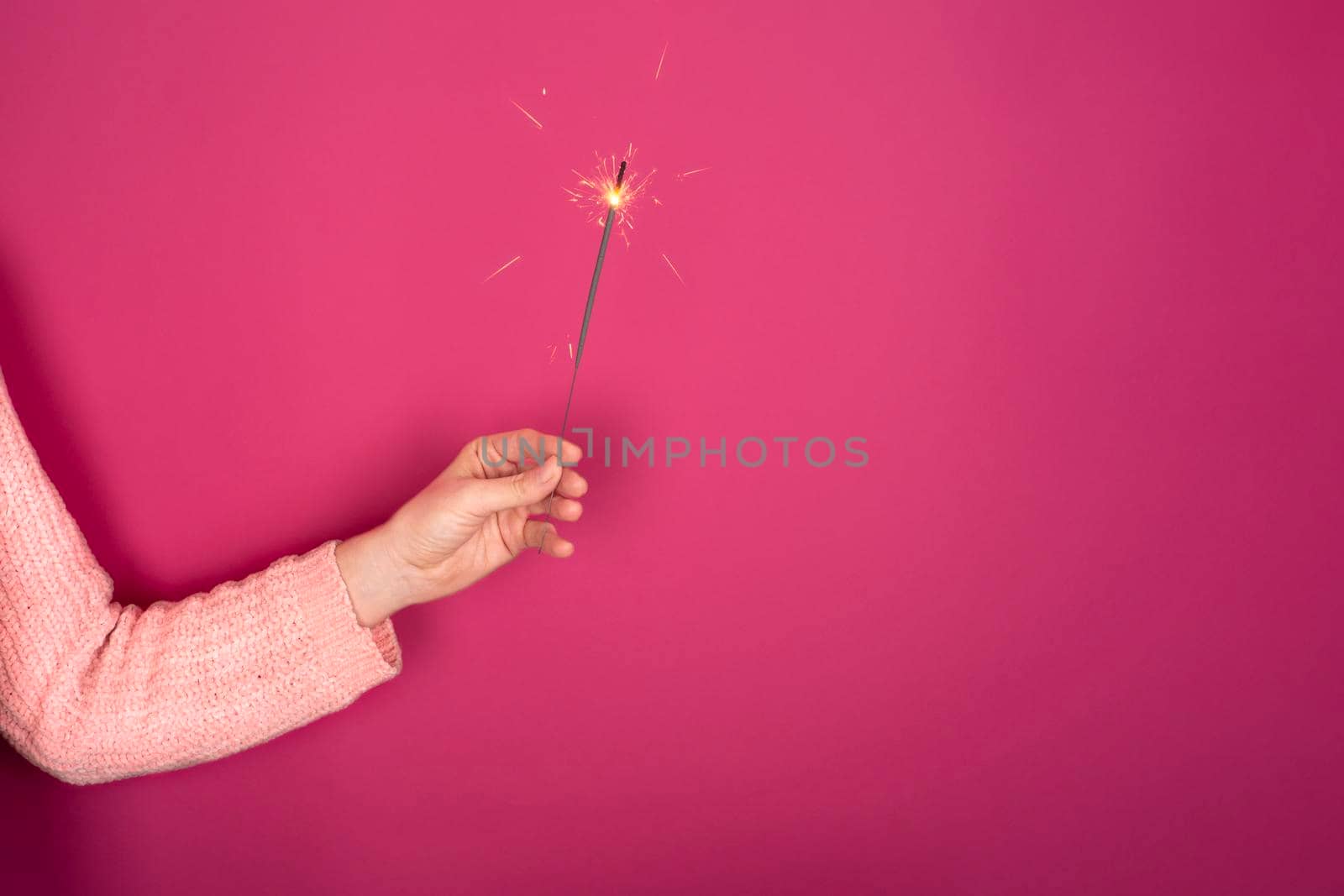 Close up of female hand with burning Christmas sparkler on pink background. Happy New Year celebration concept . Copy space.
