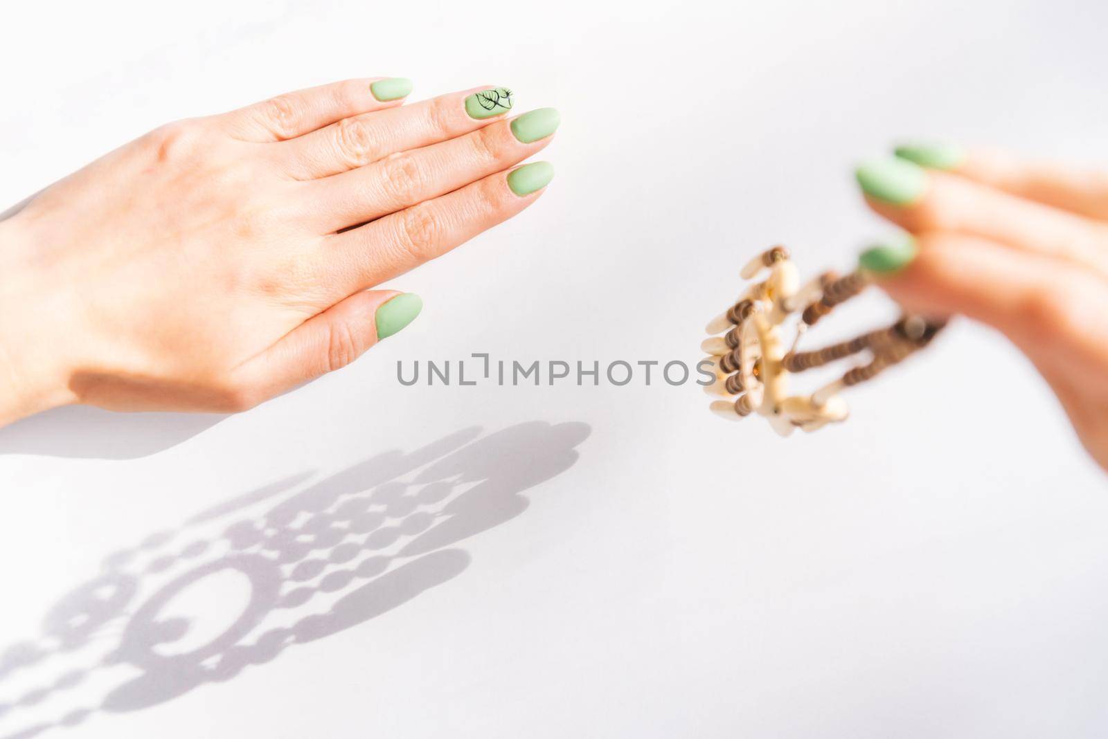 Woman’s hands with beautiful green manicure holding wooden necklace. by alexAleksei