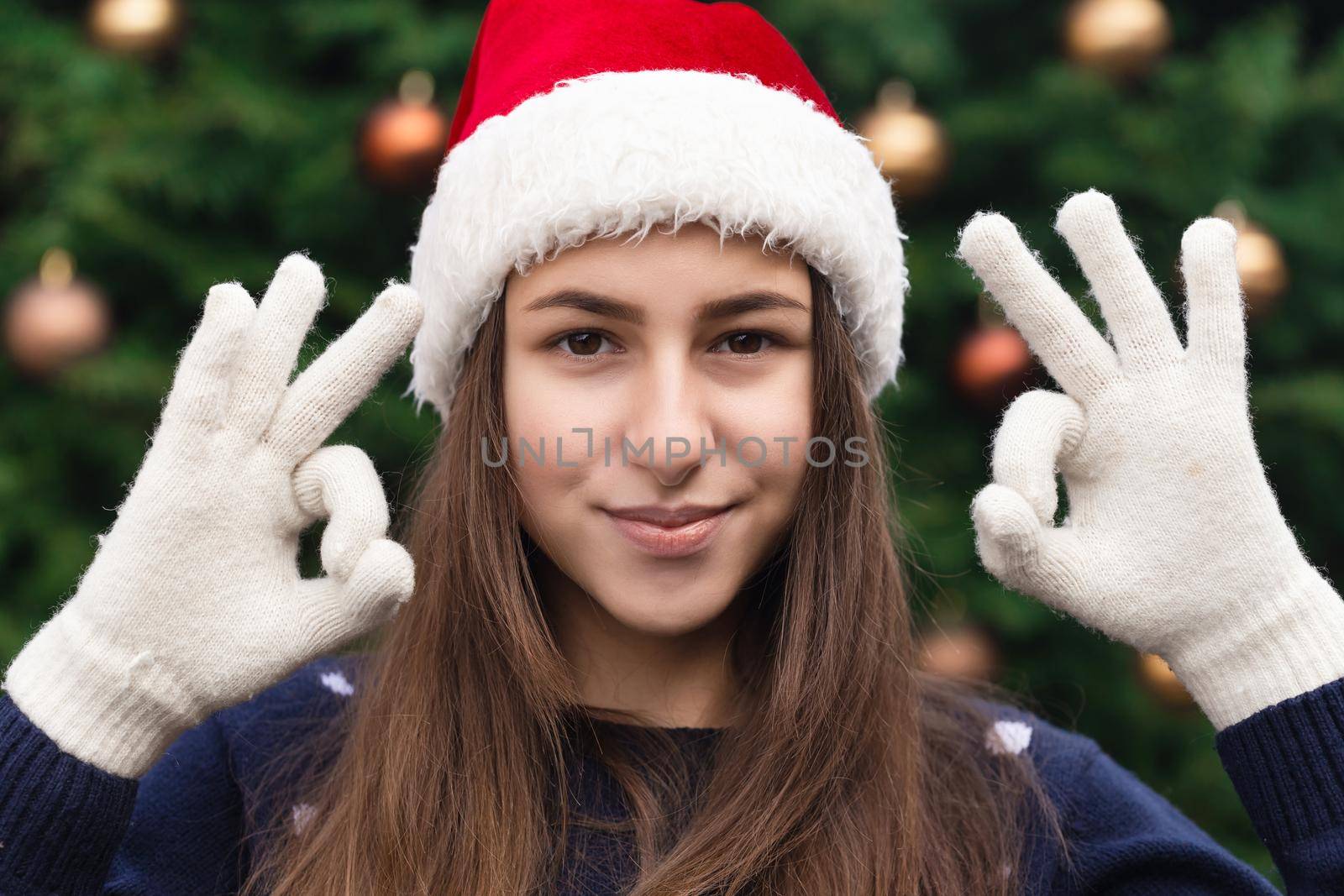 Everything will be fine for christmas. Close up Portrait of woman wearing a santa claus hat with emotion. Against the background of a Christmas tree.