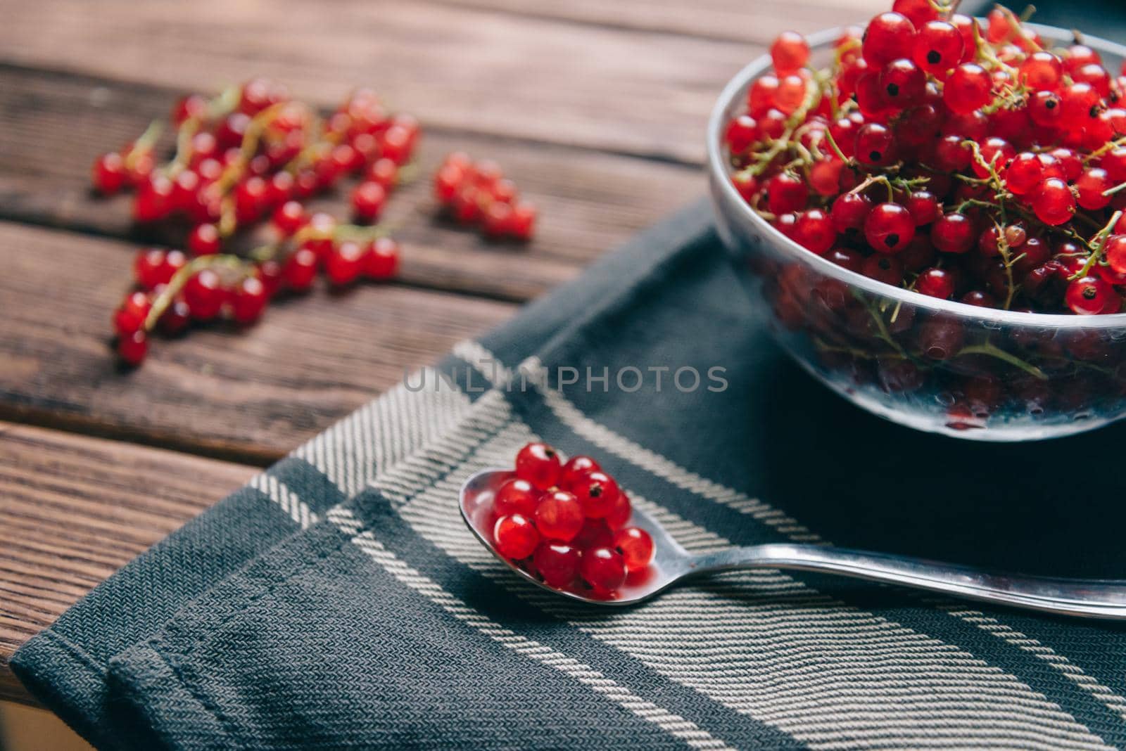 Fresh red currant in a glass bowl and on spoon on napkin.