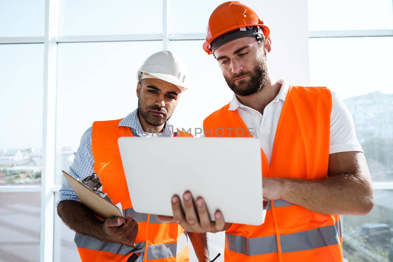 Two specialists supervisors in hardhats using laptop at construction site for work, close up