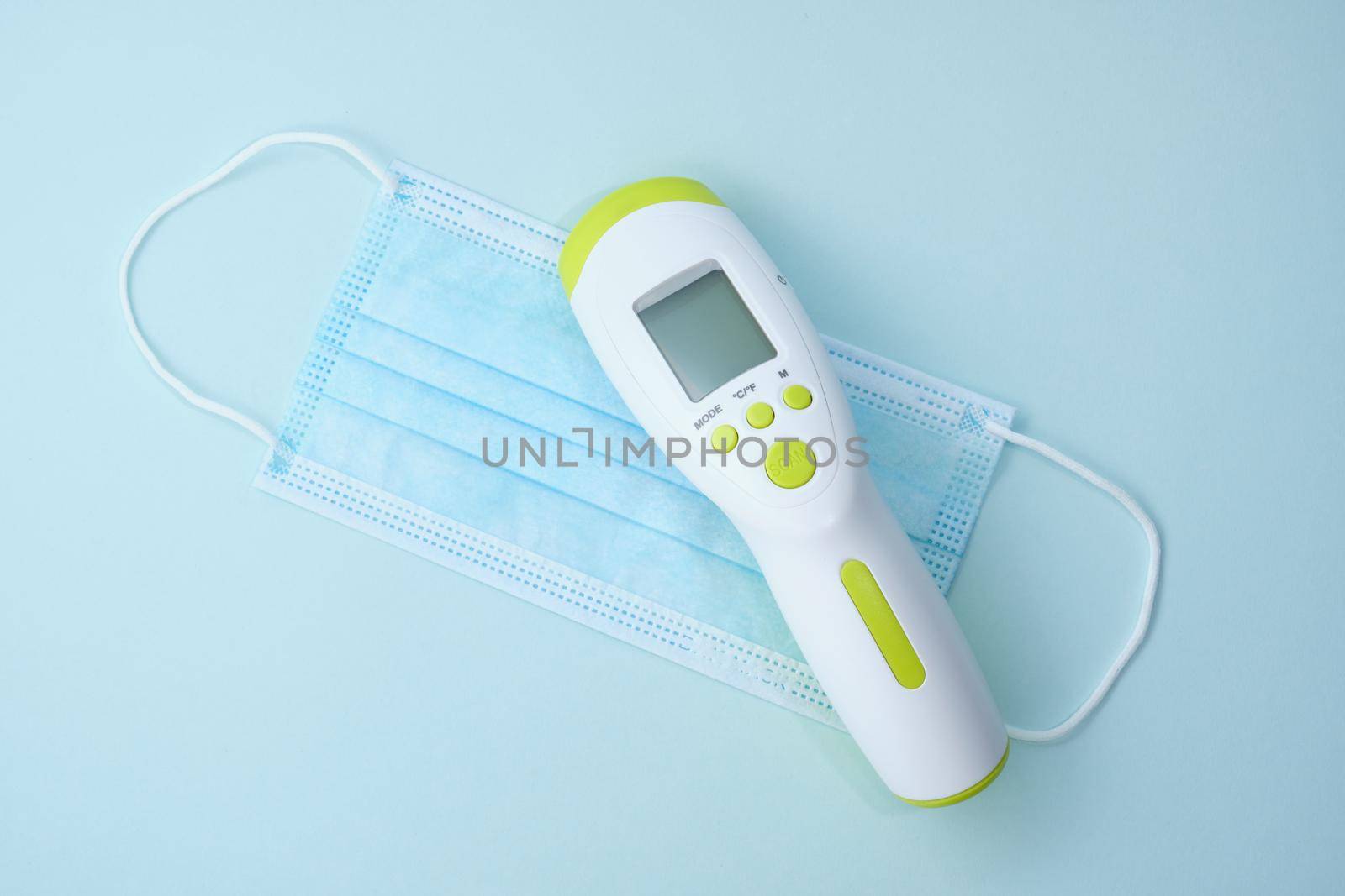 Digital medical infrared non contact thermometer gun for measuring temperature, face mask on blue background for coronavirus COVID-19 testing. Medicine concept.
