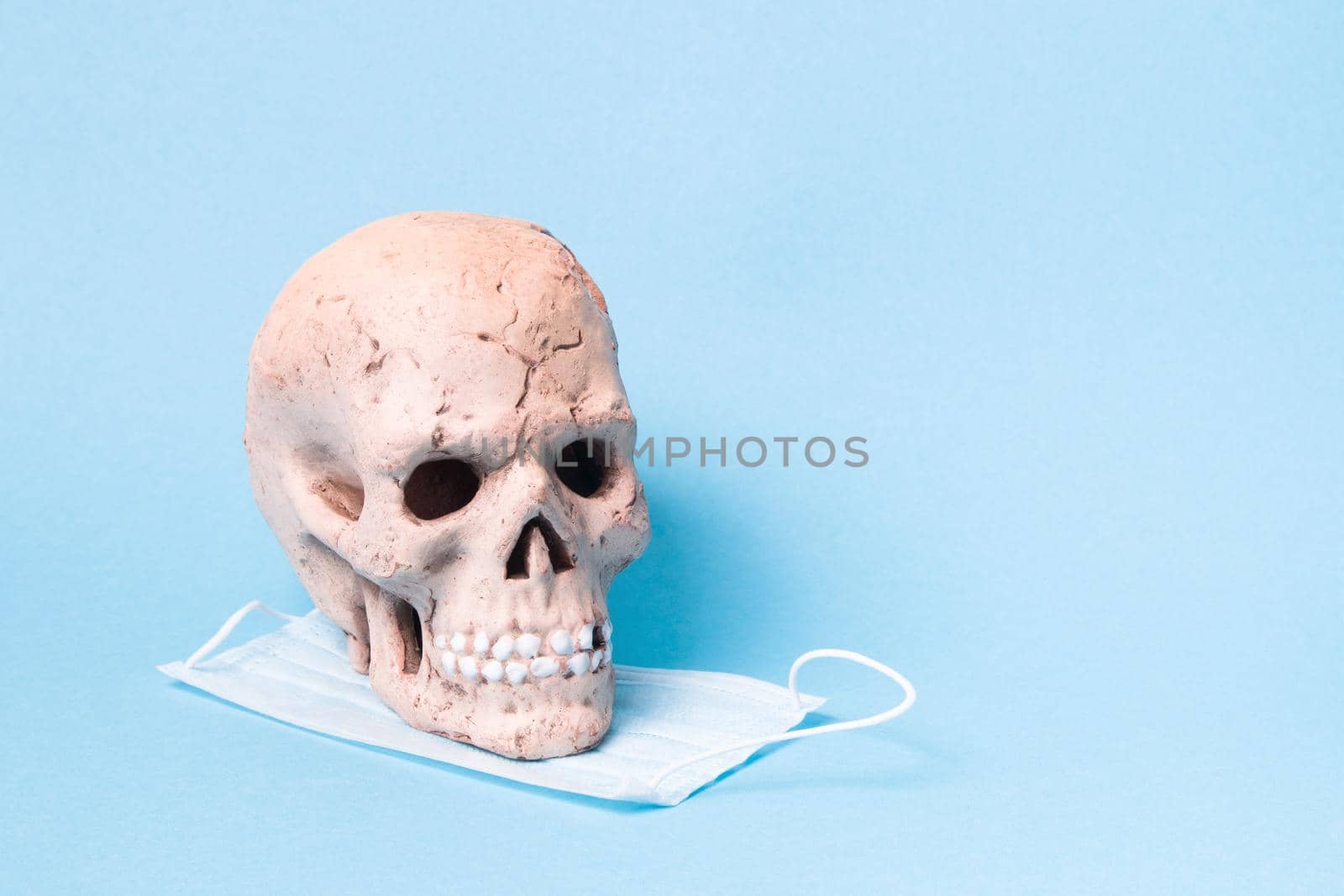 ceramic skull and blue protective medical face mask on a blue background, copy space