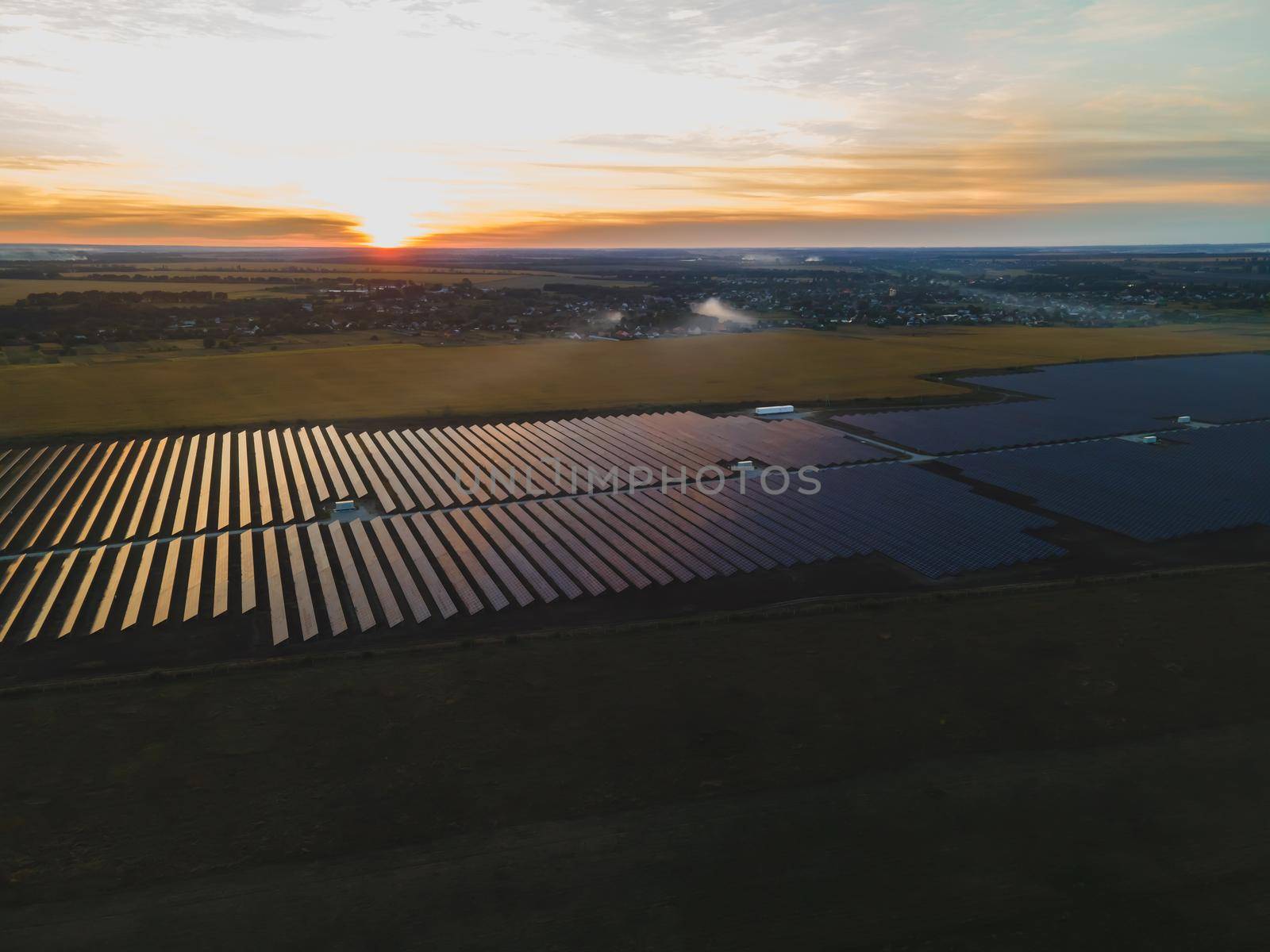 Aerial drone view into large solar panels at a solar farm in large field on countryside at bright sunset. Solar cell power plants, colorful photo