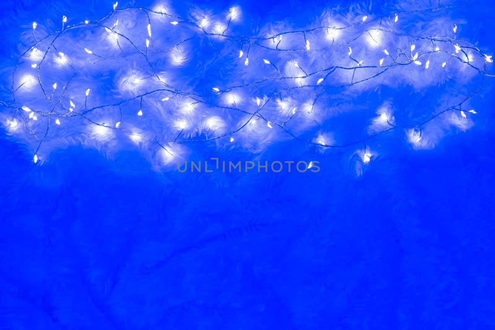 Christmas lights over a bright fluffy blue background. Yellow cozy christmas lights background. Modern scandinavian cozy new year background with copy space