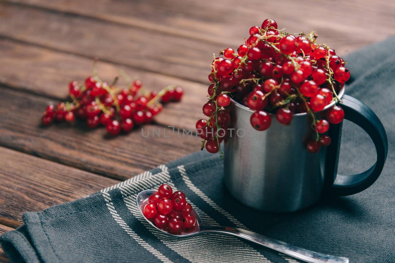 Fresh red ripe currant in a metal cup and on spoon on napkin.