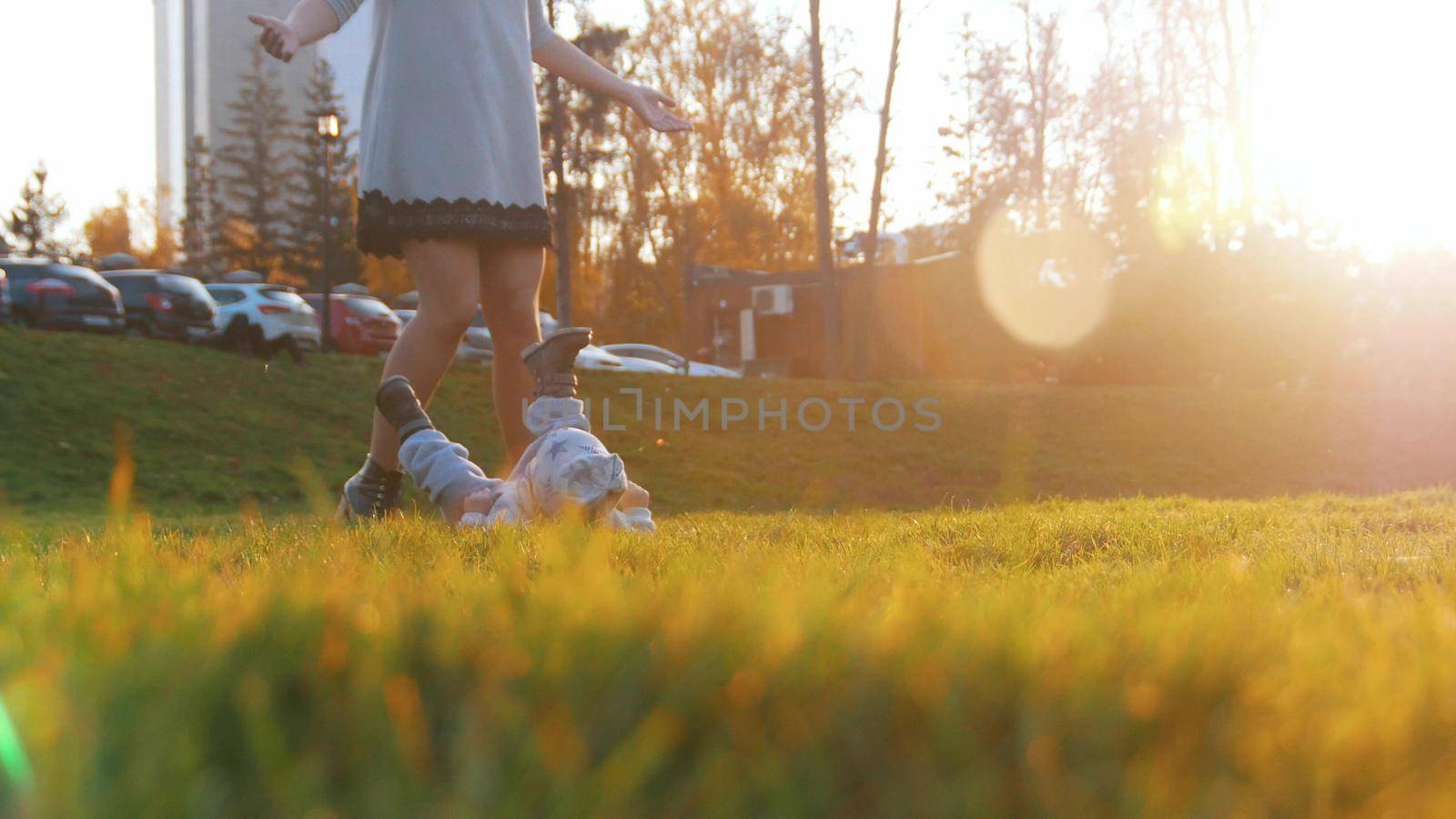 Young happy mother and her little baby boy playing in park. The baby lying on the grass. Wide shot