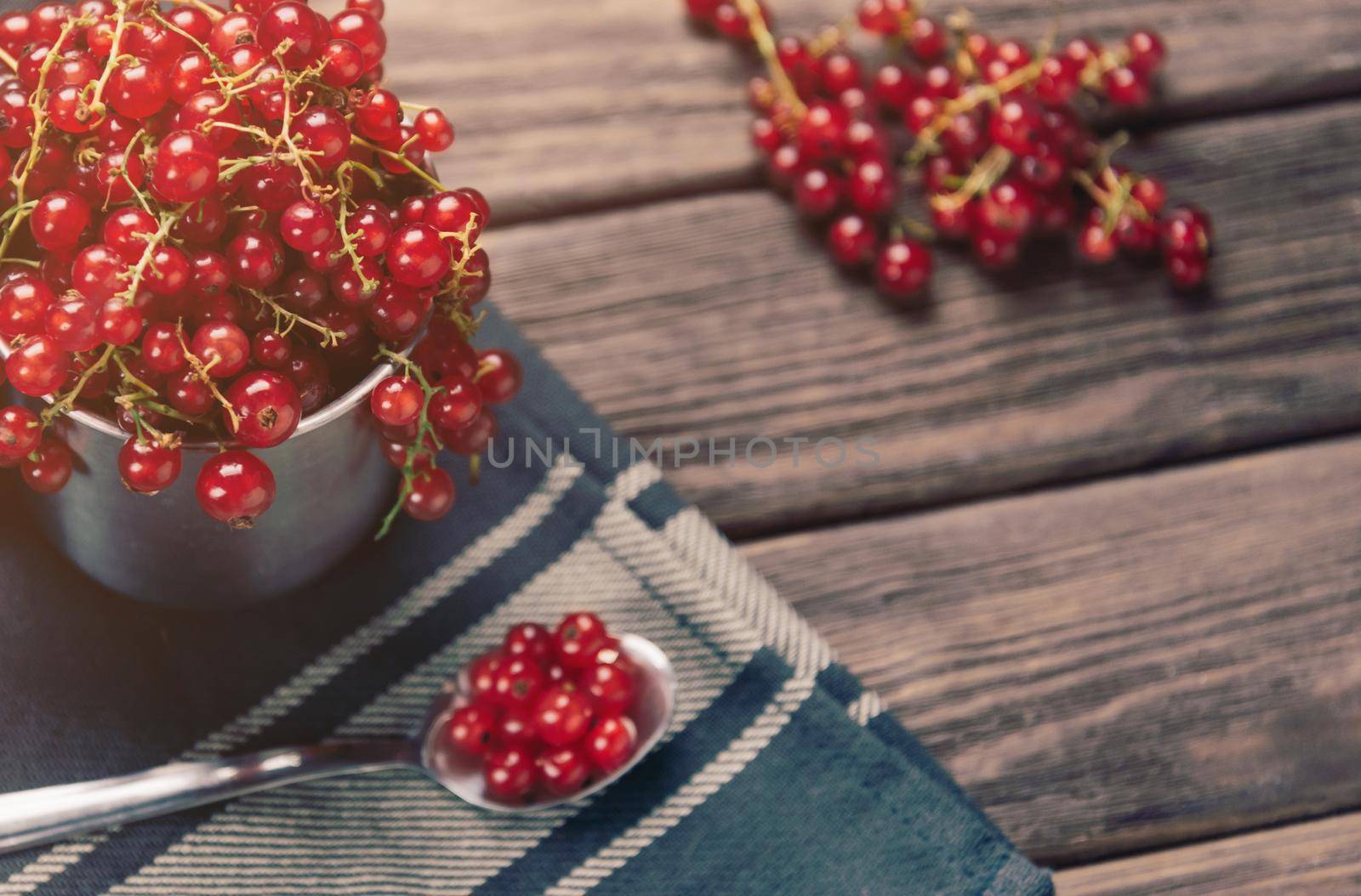 Fresh berries red currant in a cup and on spoon on wooden table.