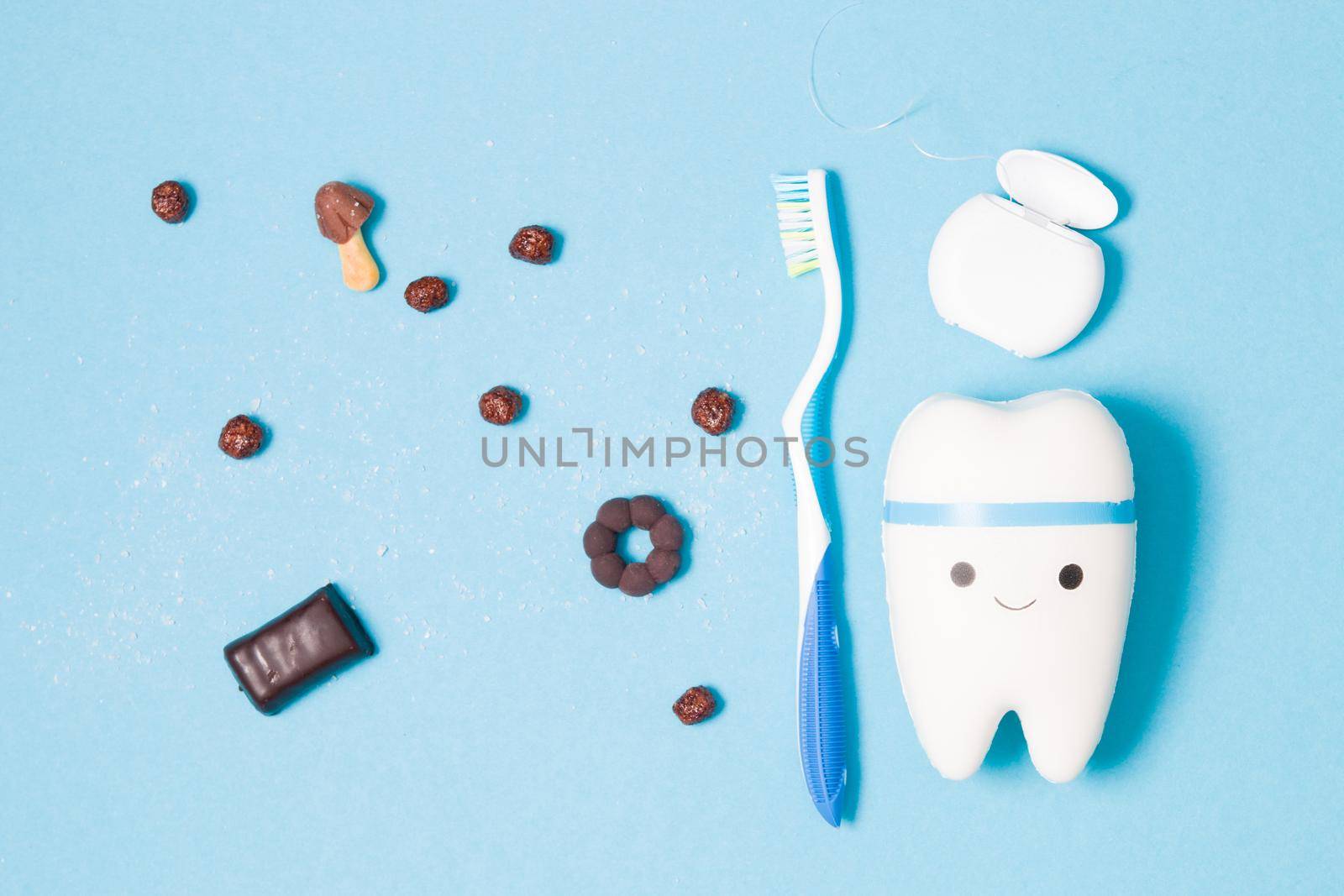 sweets, toothbrush, dental floss and toy tooth on a blue background, tooth model with a smile, protection of the oral cavity from caries concept, pediatric dentistry advertising