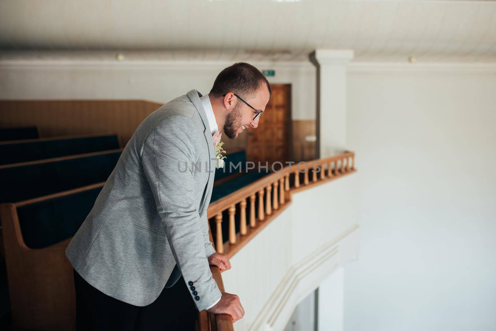 Wedding photo of emotions of a bearded groom with glasses in a gray jacket in the church building.