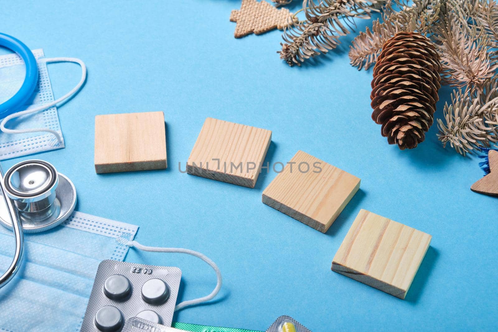 christmas decoration fir branches, fir cones, stethoscope, medical protective masks and various medicines and four wooden squares for writing year on blue background, 2021 concept by natashko
