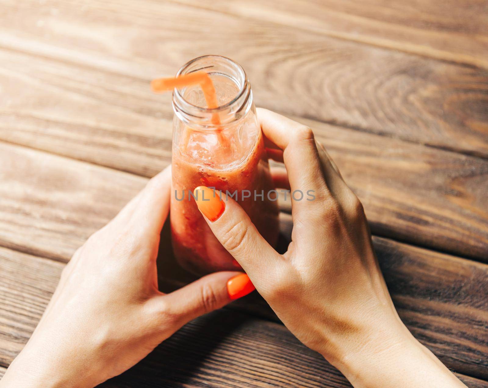 Young woman holding bottle of fresh berry smoothie with tube at wooden table. Point of view in first person.