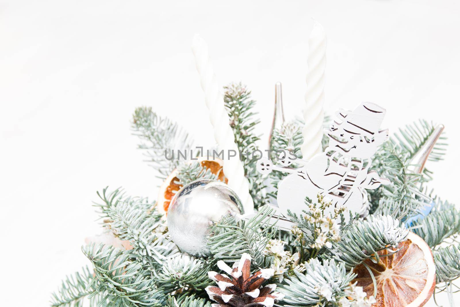 a bouquet of fir branches reinforced with a snowman, Christmas toys, dried oranges and white candles. christmas bouquet, copy place, light background by natashko