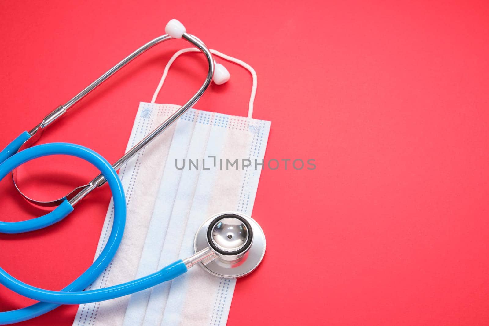 medical protective disposable mask and stethoscope on red background copy space