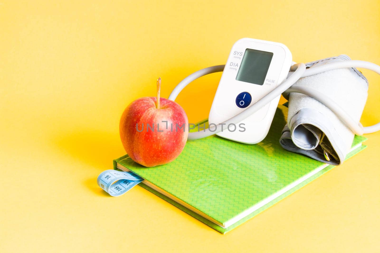 blood pressure monitor on a green notebook, a red apple and a notebook with a bookmark from a measuring blue tape, weight loss and health care, proper nutrition concept by natashko