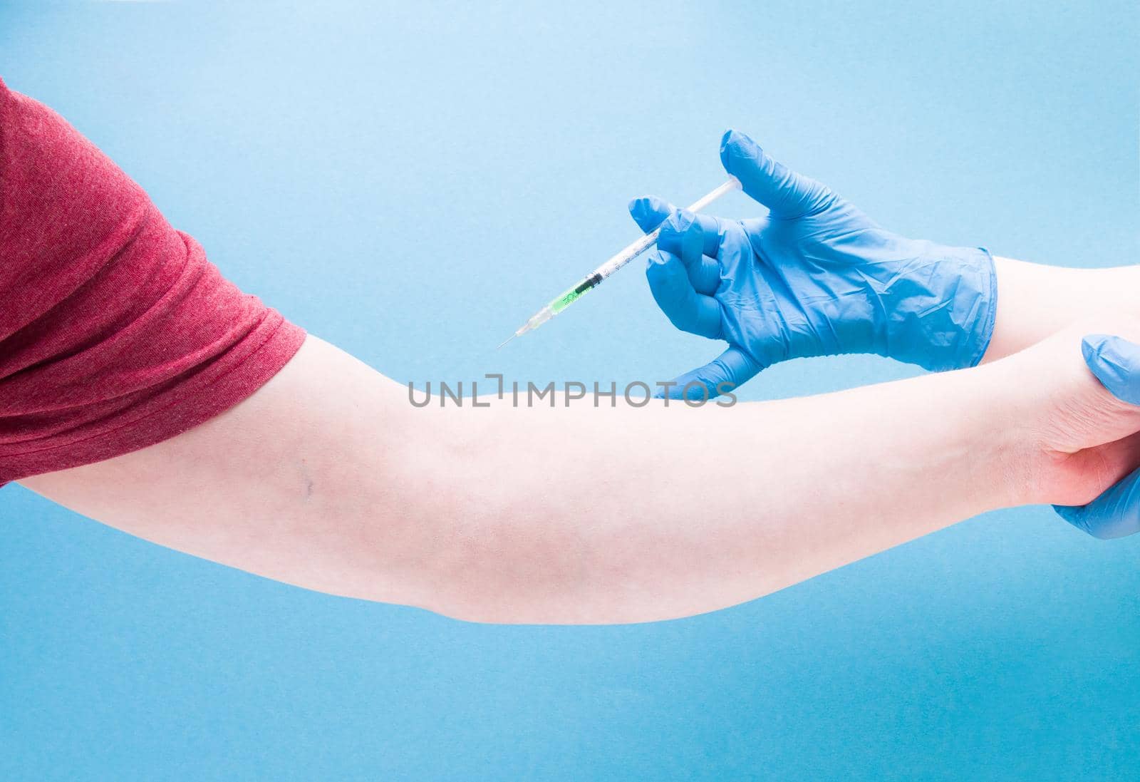 female hand in a blue rubber medical glove injects a male insulin syringe with a green vaccine on a blue background copy space, treatment and health care concept, stop coronavirus