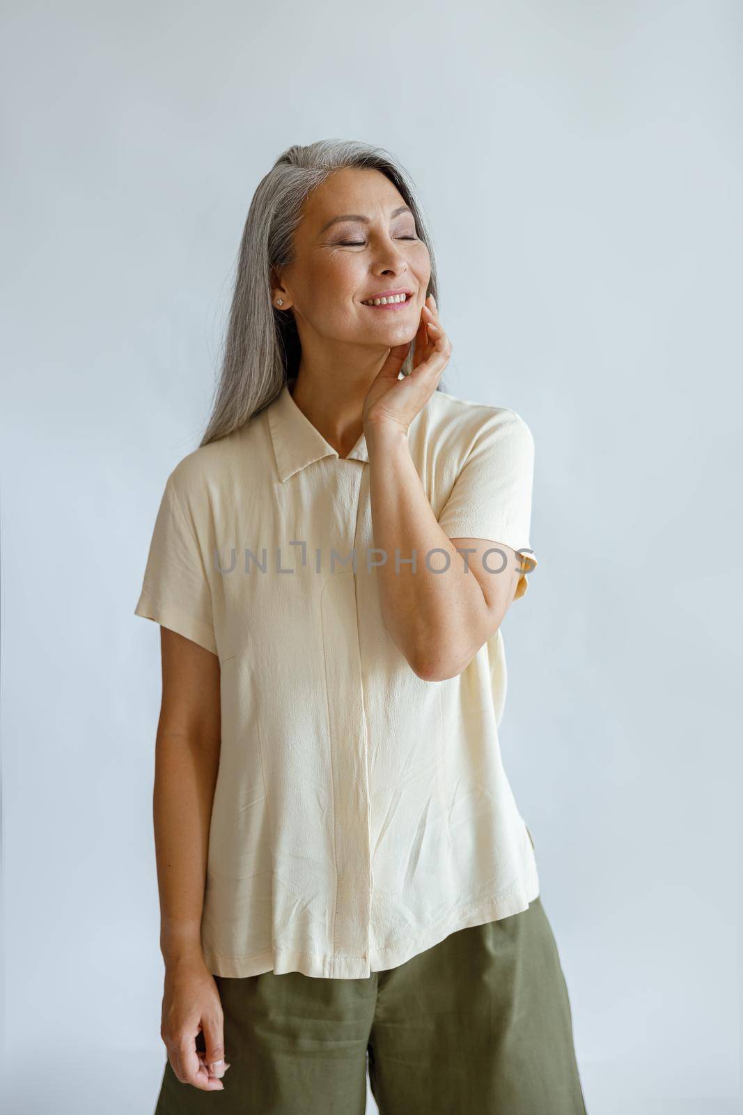 Cheerful silver haired lady in stylish casual outfit poses for camera on light grey background in studio. Mature beauty lifestyle
