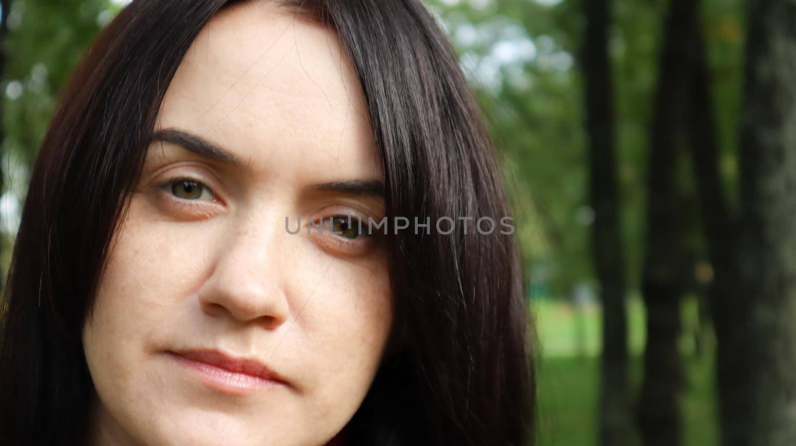 Close up portrait of beautiful caucasian woman while walking outdoors in city park with blurred background. A woman is looking at the camera on a sunny day. by Roshchyn