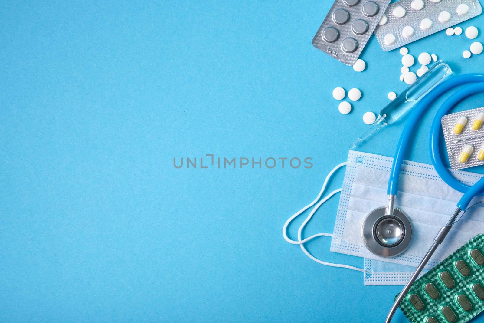 stethoscope, protective medical mask and various medications on a blue background copy space by natashko