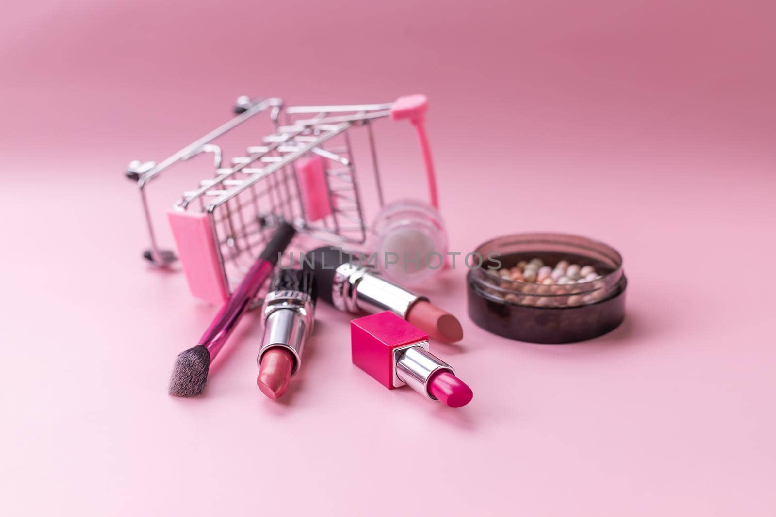 Creative concept with shopping trolley with makeup on a pink background.