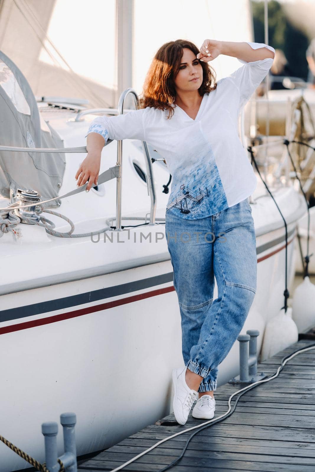 a happy woman with long hair stands on the pier near the yacht.
