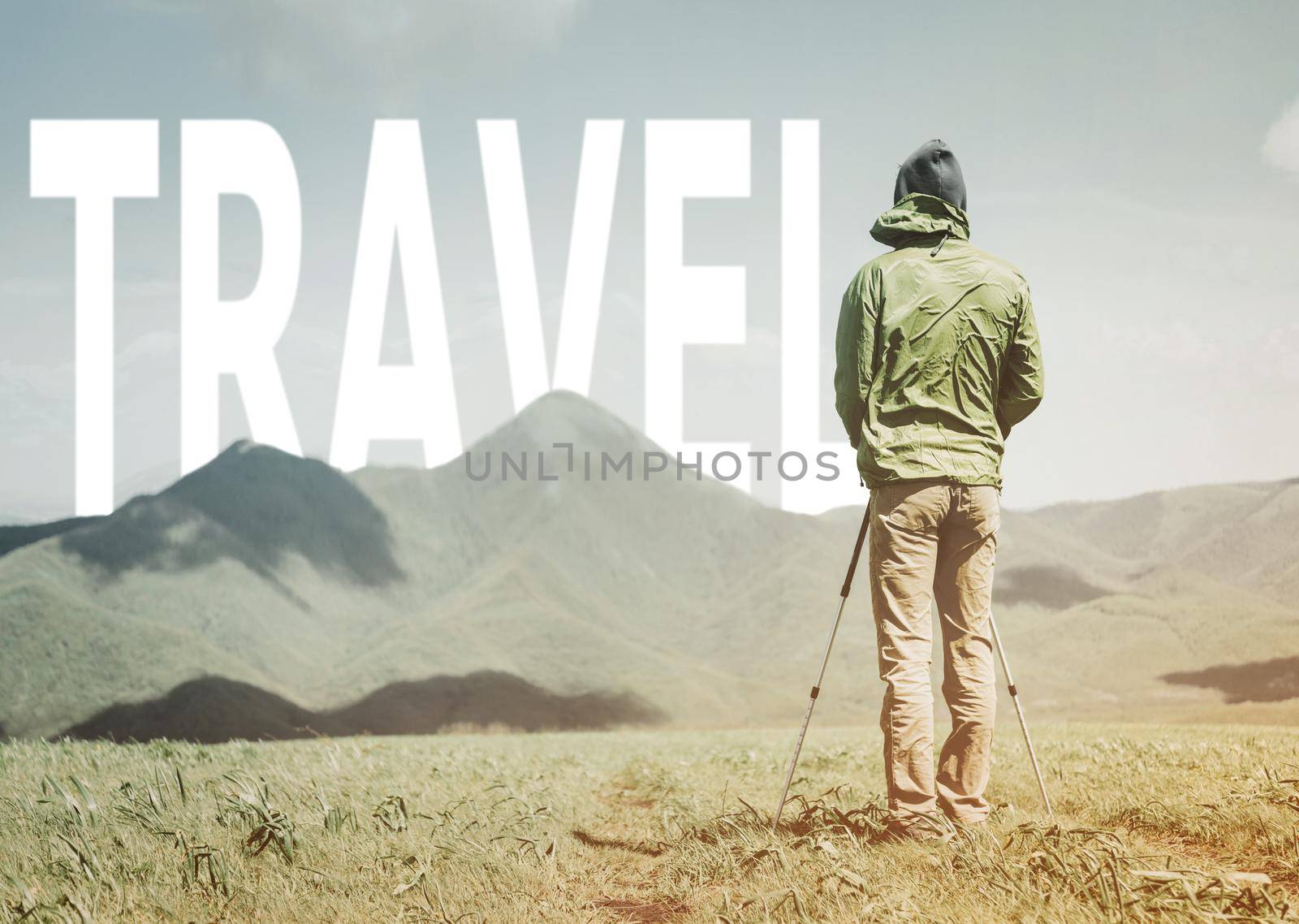 Explorer young man with trekking poles standing in front of word travel over mountain ridge in summer outdoor.