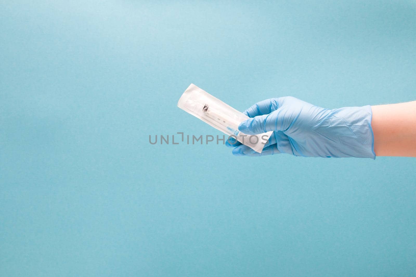 female hand in a blue disposable medical glove holds a disposable syringe in a package, blue background copy space by natashko