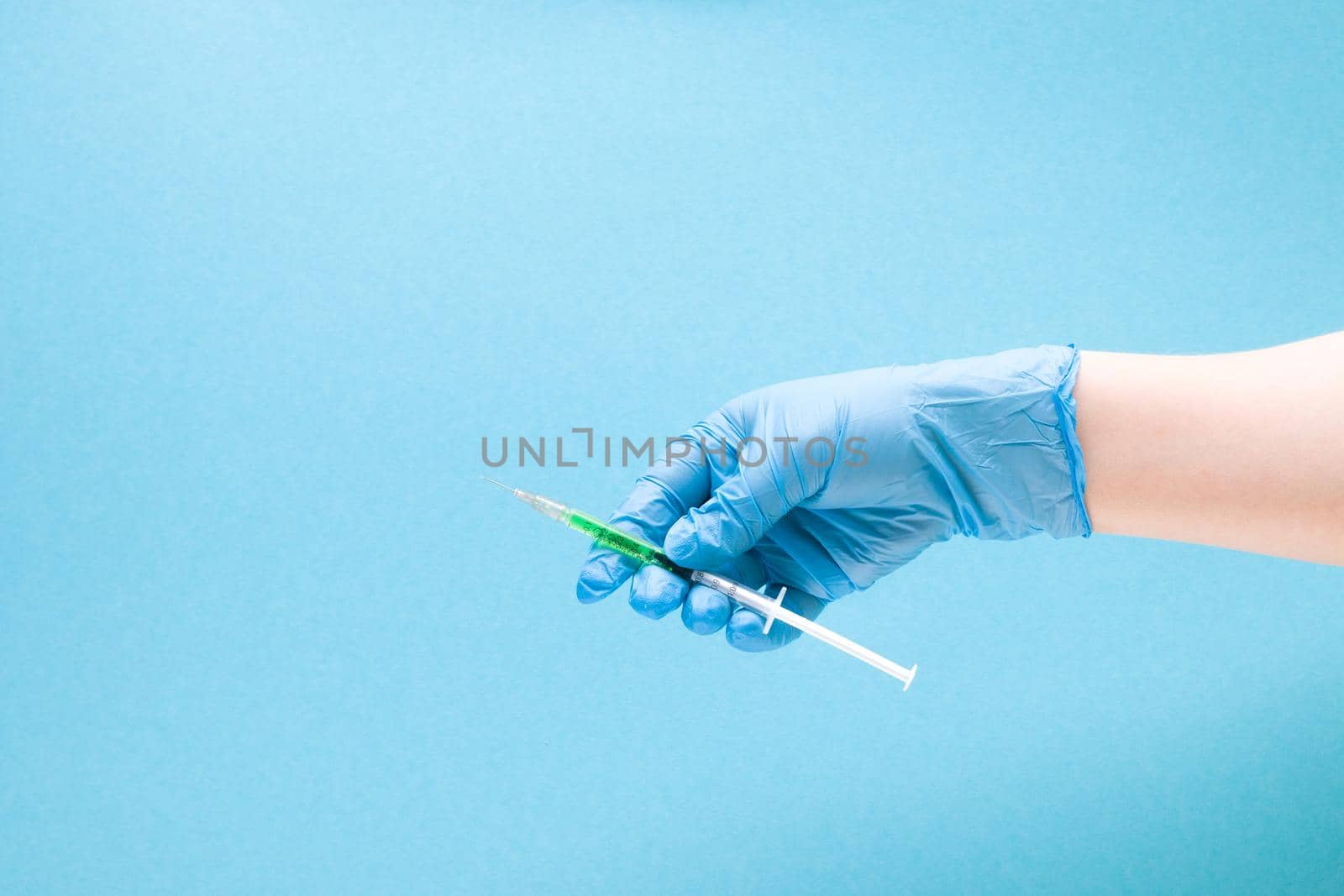 female hand in a blue rubber medical glove holding an insulin syringe with green medicine inside on a blue background copy space, treatment and health care concept, diabetes concept