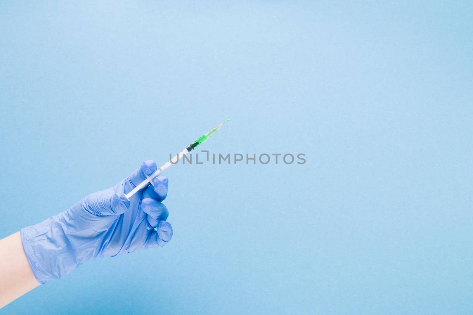 female hand in a blue rubber medical glove holds an insulin syringe with green colored medicine, the vaccine inside on a blue background copy space, treatment and health care concept, diabetes concept