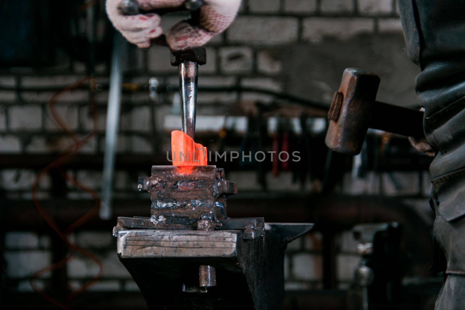 Workspace of blacksmith. Blacksmith working with red hot metal at anvil in a forge. Portrait