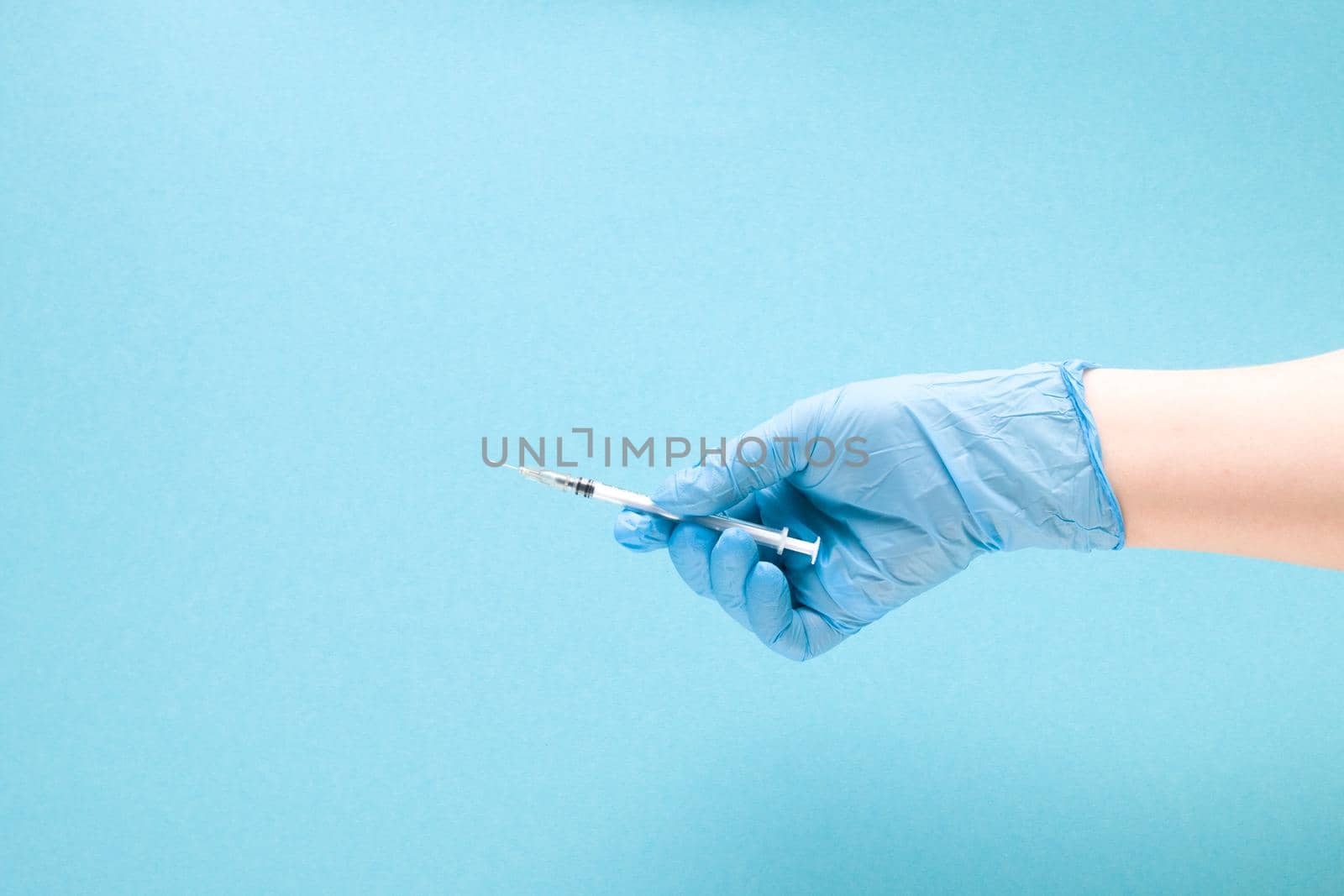 female hand in a blue rubber medical glove holds an insulin syringe on a blue background copy space, treatment and health care concept, diabetes concept