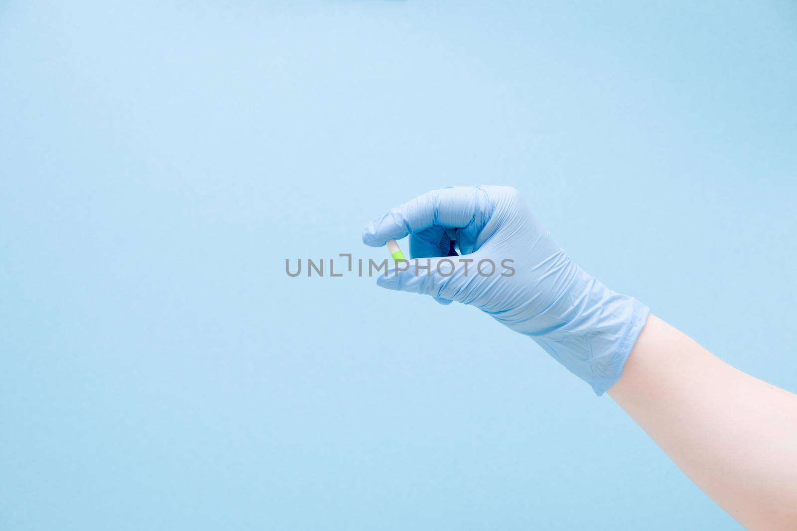 a female hand in a blue rubber medical glove holds a capsule tablet on a blue background copy space, tablet of blue and green color, treatment and health care concept