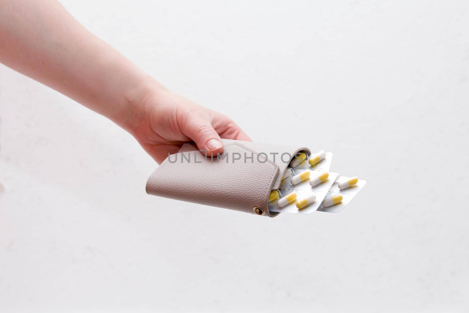 female hand holds a purse. medicine pills in a closed wallet, white background